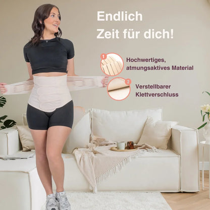 Frau mit Bauchgurt nach der Geburt im Wohnzimmer – zeigt den Gurt im Alltag.  